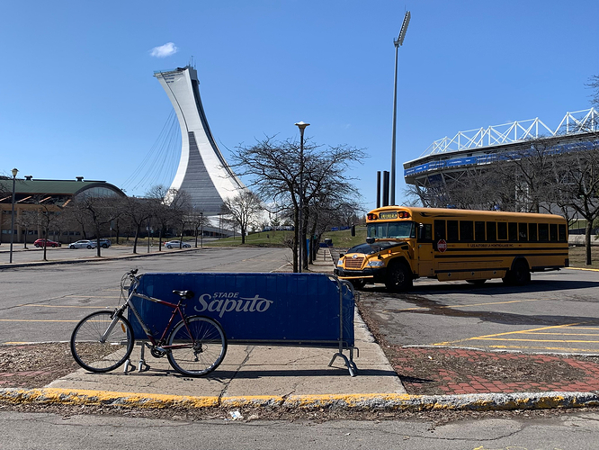 my bike on a portable railing in a parking lot; there's a school bus there, and Saputo Stadium on the right, and the Olympic Stadium on the left.