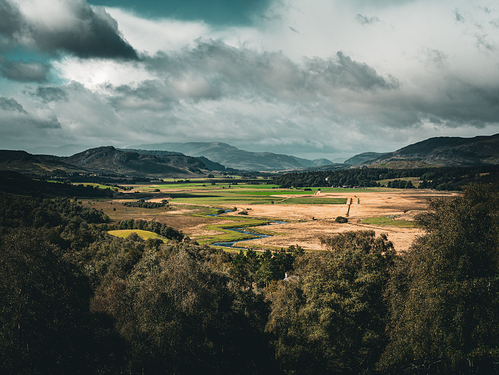 photograph of the Scottish Highlands, beautifully illuminated with light across green and golden fields.