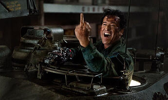 Bruce Campbell as Ash stands in the hatch of a tank, defiantly raising a middle finger to an unseen adversary