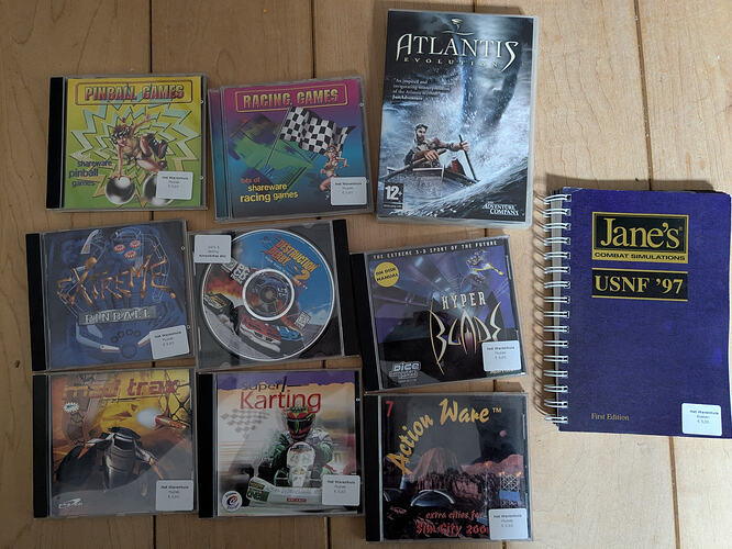 Several cd roms and a DVD case of shareware collections, racing games, and adventure games, and a spiral bound manual for Jane's Combat Simulator.