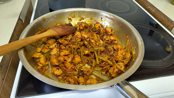 a beautiful stainless steel pan filled with a delicious chicken stir fry. It's atop a tiny stove in a visibly too large and unsightly gap in the counter
