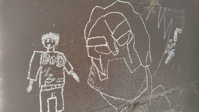 Photograph of some graffiti on a wall constructed of painted breeze blocks. It shows a figure wearing a shirt adorned with the moniker "Bob" standing before a giant head wearing a mask highly reminiscent of that worn by MF DOOM.