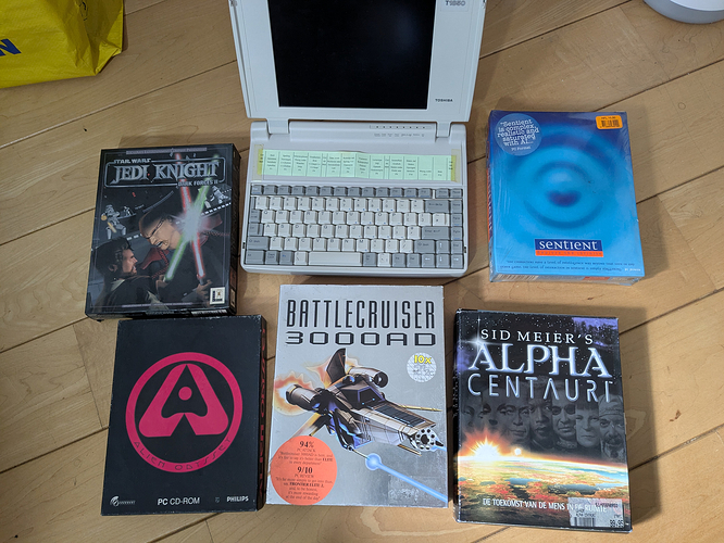 Picture of five big box PC games: Star Wars Jedi Knight: Dark Forces II, Sentient, Alien Odyssey, Battlecruiser 3000AD, and Sid Meier's Alpha Centauri. In the middle is an old early 90s Toshiba laptop.
