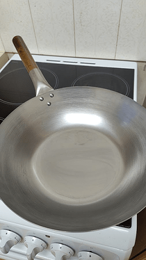 and enormous carbon steel flat-bottomed wok on a very cheap stovetop. It's unseasoned, and gleams in the light