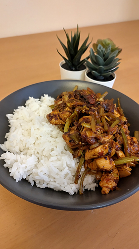 a chicken stir fry with a lovely red-orange hue. It contains strips of celery, spring onion, pickled ginger and hot broadbean paste, amongst other things. A trip of fake plants is used to add a little interest to the background