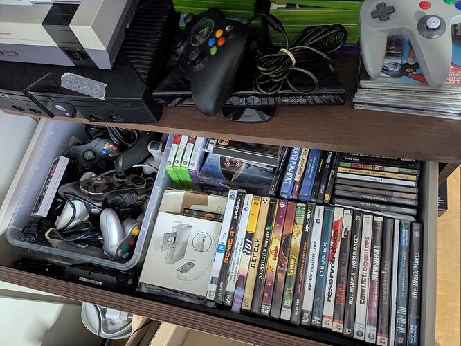 An open drawer showing more DVD case of mostly PC games, some Dreamcast cases, some CD-ROM cases, and a plastic box full of controllers.