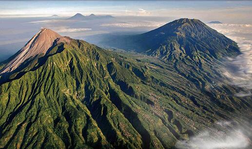 Indonesian volcanoes, photographed from the air. They stand tall and imposing, surrounded by blankets of cloud.